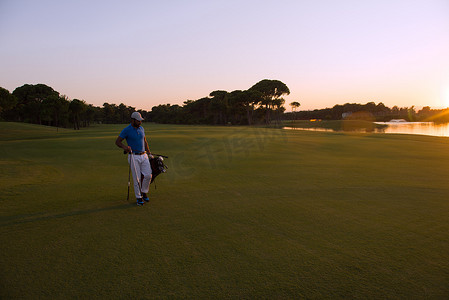 高尔夫球手在美丽的日落时行走并携带高尔夫球包