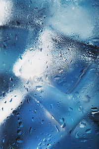蓝色背景上装有清爽冰水的玻璃杯中的冰块。