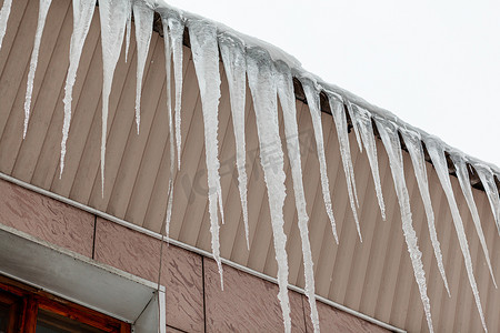 冷行人摄影照片_建筑物的屋顶上悬挂着又大又长的冰柱。