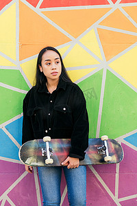 玩滑板的女子摄影照片_色彩缤纷的墙壁上玩滑板的年轻女子