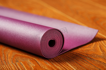 淡紫色的瑜伽垫卷成一卷铺在木地板上。