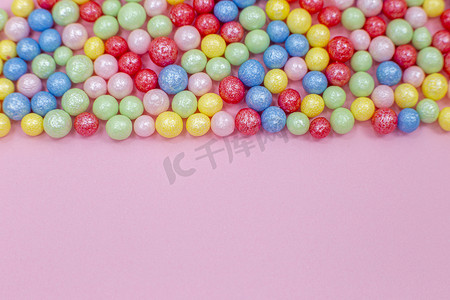 粉红色背景的顶部是多色圆形光泽糖果配料球。