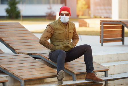抵御病毒摄影照片_坐在木制躺椅上的家伙戴着墨镜和面罩来抵御病毒