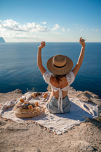 街拍照片上，一位美丽的女人，黑发，白上衣，短裤，戴着帽子，在俯瞰大海的山上野餐