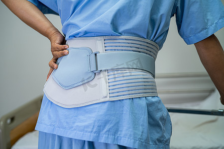 半截皮带摄影照片_亚洲女性患者佩戴背痛支撑带，用于带助行器的骨科腰椎治疗。