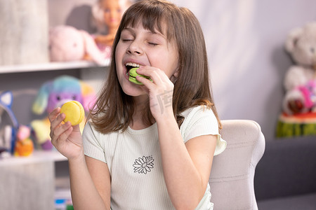 小女孩柠檬摄影照片_年轻的黑发小女孩无法做出正确的决定和选择先咬什么马卡龙-左边是柠檬和绿柱石馅料，右边是开心果奶油，然后咬绿色的马卡龙