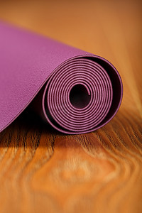 淡紫色的瑜伽垫卷成一卷铺在木地板上。
