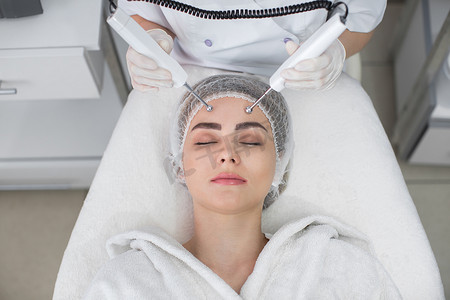 在水疗中心进行美容电镀美容治疗的女性的宏观特写肖像。治疗师在脸上用电极施加低频电流。