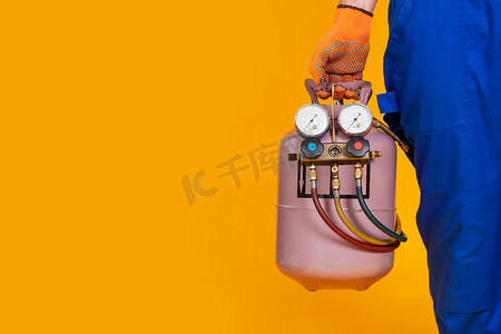 一名男空调修理工手里拿着一个氟利昂气瓶和一个压力测量传感器，用于空调加注。