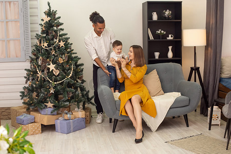 快乐的年轻家庭在家里的灰色沙发上快乐地玩耍，旁边是圣诞树