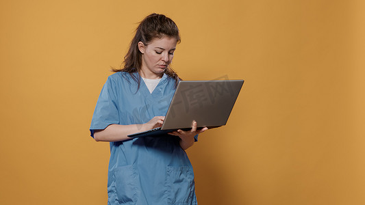 忙碌的医生站着拿着笔记本电脑并看着屏幕在键盘上打字的肖像