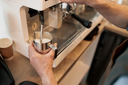 咖啡师手用蒸汽在水罐中加热牛奶的特写