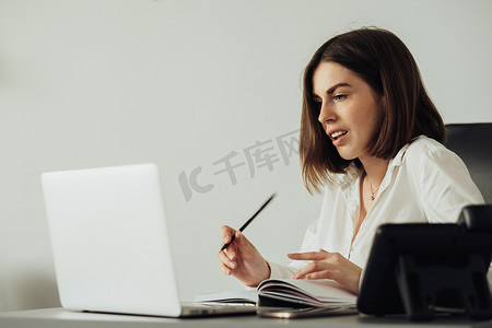 自信的年轻女性在办公室用笔记本电脑工作，女经理在工作场所写笔记本