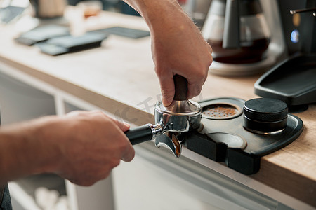 研磨咖啡摄影照片_咖啡师捣固研磨咖啡以制作浓缩咖啡的特写