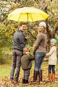 伞下的男孩摄影照片_伞下微笑的年轻家庭的后视图