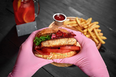 手戴粉色橡胶手套，手里拿着汉堡，配猪排、泡菜、新鲜蔬菜