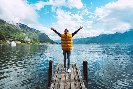 年轻女旅行者张开双臂站在木桥上，欣赏瑞士日内瓦湖的美景