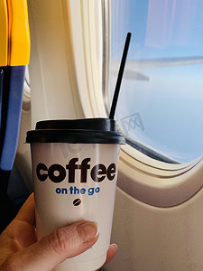 拿白摄影照片_女人在飞机上喝咖啡。女人手拿着白纸杯热咖啡在飞机上。