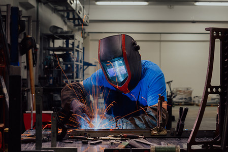 重工业工厂摄影照片_专业重工业焊工在工厂内工作，戴着头盔并开始焊接。