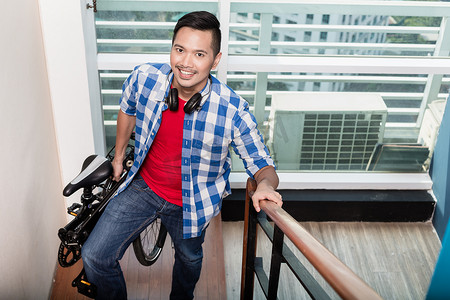 亚洲年轻男子扛着折叠自行车上楼梯到公寓