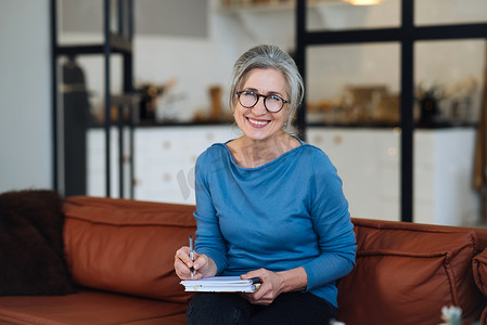 戴眼镜的快乐老年妇女在家里写笔记本