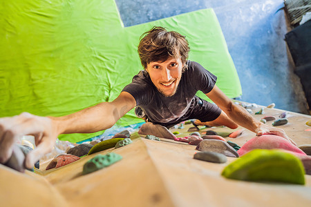 抱石摄影照片_肌肉男在室内岩墙上练习攀岩