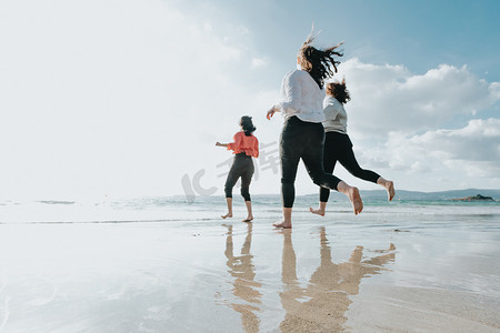 快乐的女性朋友在阳光明媚的日子里在海边跑步，朋友们在傍晚日落时快乐地在海边的海滩上玩耍放松。