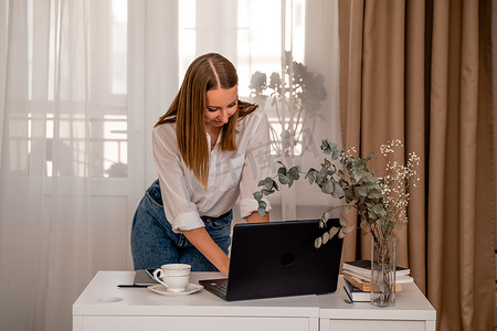 欧洲职业女性坐在家庭办公室的桌子旁，拿着笔记本电脑，一位积极的女性一边在电脑上工作一边学习。