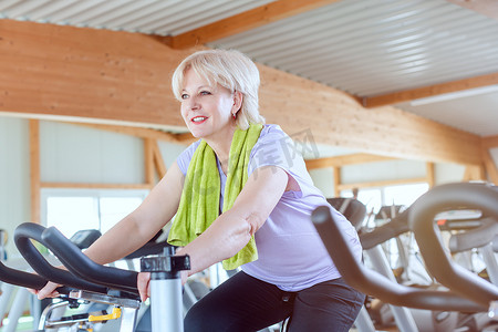 国潮蒸汽效果摄影照片_高级女性在健身房骑自行车锻炼身体以获得更好的健身效果