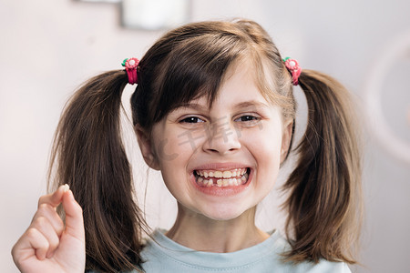 可爱小女孩的肖像很高兴，她站在卧室里，展示着她失去的乳牙，并对着无牙嘴的镜头微笑。