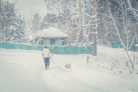 冬天遛狗摄影照片_冬天，一名妇女在村里的街道上遛狗。