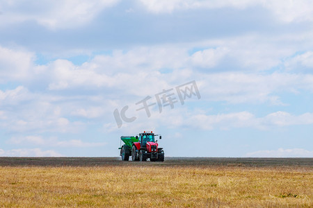 绿色拖车里的红色拖拉机正在向田地里运送肥料。
