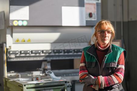 一位戴着护目镜站在数控机床前、在现代化金属生产加工厂工作的妇女的肖像