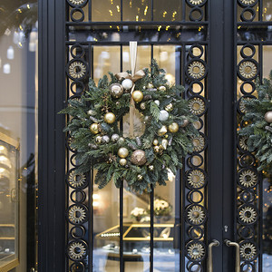 圣诞摄影照片_冷杉树枝的圣诞花环，装饰挂在透明门上，门上有金属嵌件