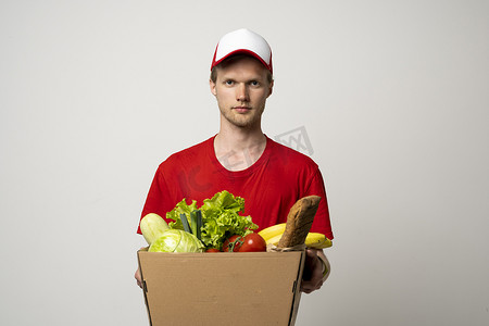 身穿红色制服的送货员拿着工艺纸包，里面装着白色背景、工作室肖像上隔离的食物。