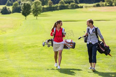 夫妇背着高尔夫球包在高尔夫球场散步