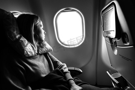 乘飞机旅行时，疲惫的金发休闲白人女士睡在座位上。