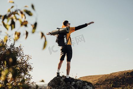 背着背包的旅行人的后视图，日落时站在岩石顶上，男性游牧者享受自由，单独旅行的概念