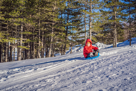 趣味摄影照片_快乐积极的小男孩享受雪橇和寒冷的户外天气，冬季趣味活动概念