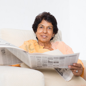 黑色沙发摄影照片_印度成熟女人读报纸