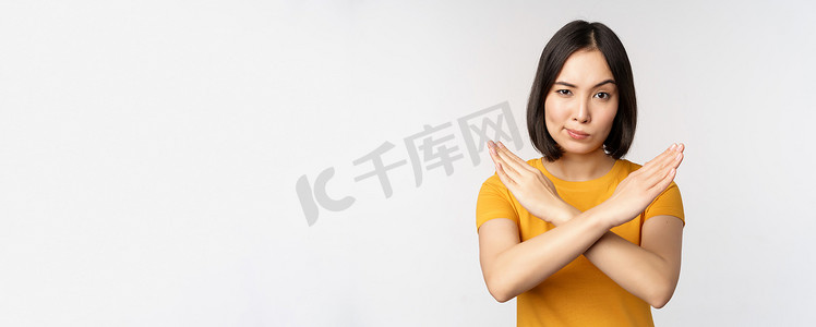 亚洲女性的肖像看起来严肃而愤怒，展示停止禁止手势、禁忌标志、禁止某物、站在白色背景上的黄色 T 恤