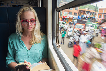 金发白种女人在火车上靠窗看书。
