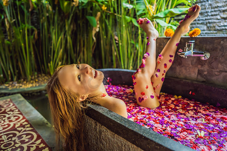 有魅力的年轻女子在沐浴着热带花卉和芳香油的花瓣。