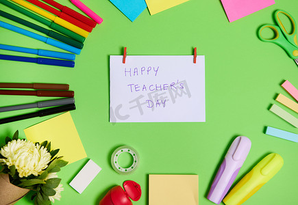 色彩缤纷的文具办公用品和学校配件的顶部视图排列成圆圈，中间是白纸，上面写着“教师节快乐”