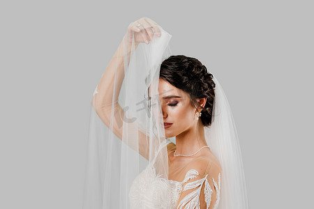 穿着婚纱的年轻漂亮新娘在工作室里触摸白色背景的新娘面纱。