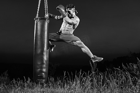 体育锻炼黑白摄影照片_一名男拳击手用沙袋训练的单色照片