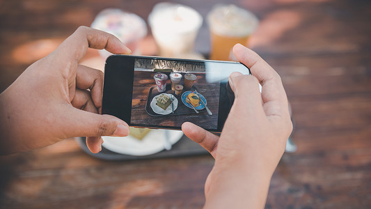 女人双手用手机拍摄食物照片，顾客女人使用智能手机拍摄食物照片，以便在咖啡馆和餐厅店与朋友分享。