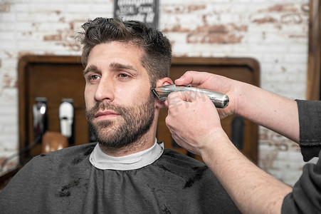 剪头发摄影照片_男理发师在理发店用剪刀给男性顾客剪头发。