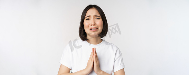 绝望哭泣的亚洲女性乞求、寻求帮助、恳求并说请，站在白色背景的白色T恤上