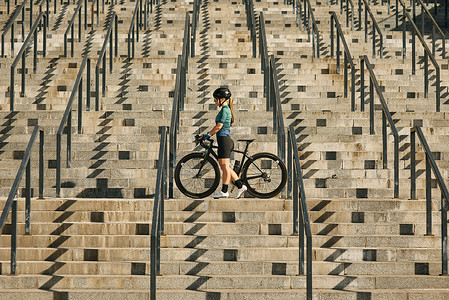 穿着自行车服和防护装备的年轻职业女自行车手在城市骑行训练后站在台阶上